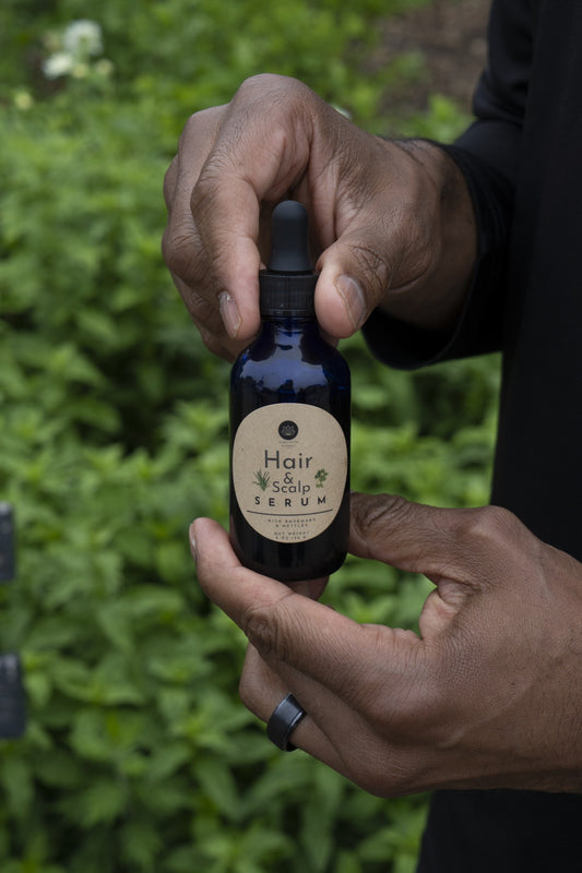 Person holding a bottle of Hair Scalp Serum with a blurred green background