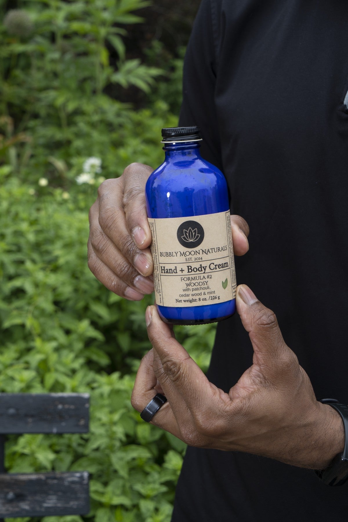 Blue Colbalt bottle being held with two hands with green background.