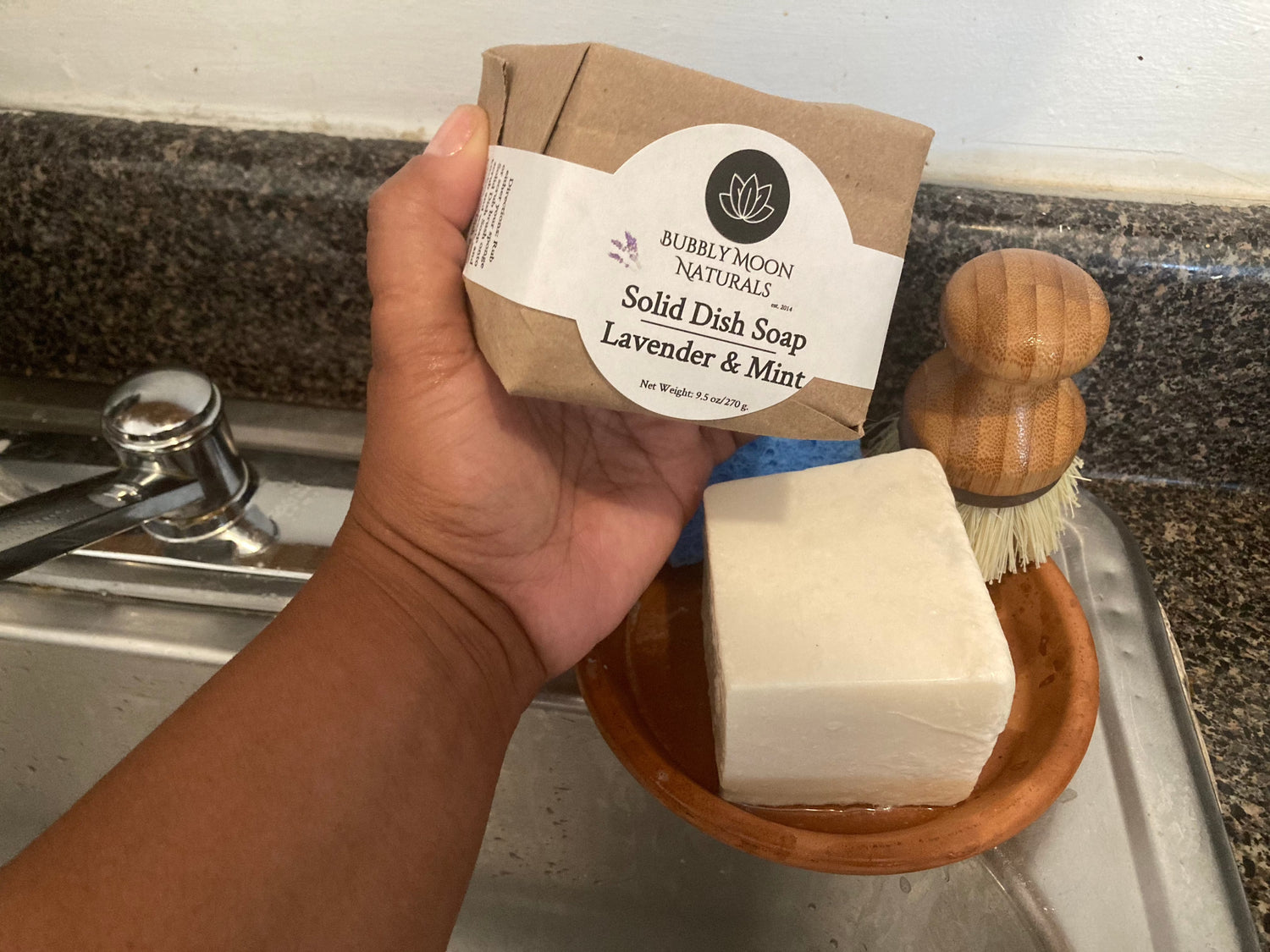 Solid Dish Bar Lavender & Mint being held in hand with white label and packaged in brown paper