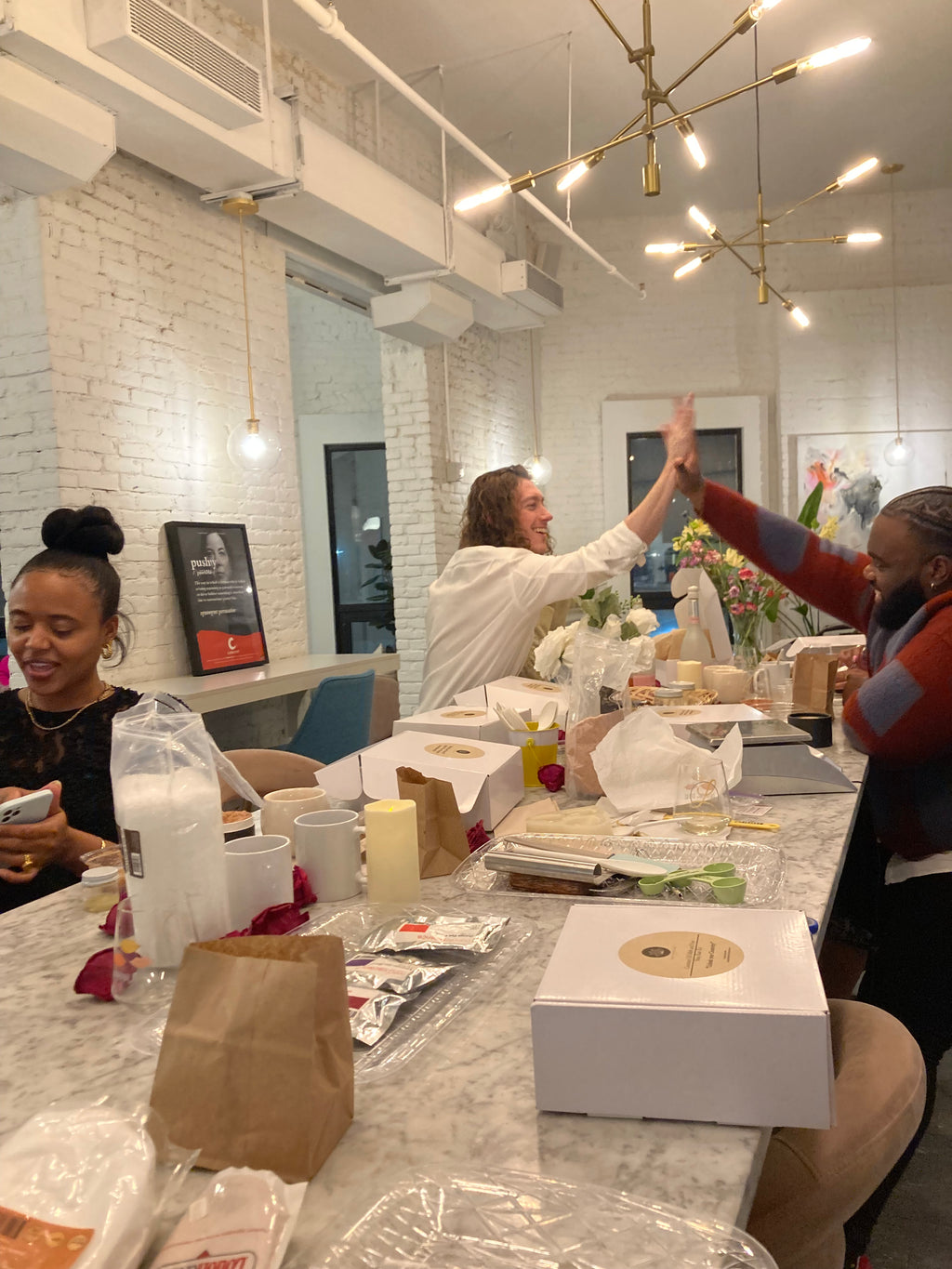 Men hi-fiving with boxes of Bubbly Moon Naturals' materials and supplies on table for natural soap making and herbal scrub making